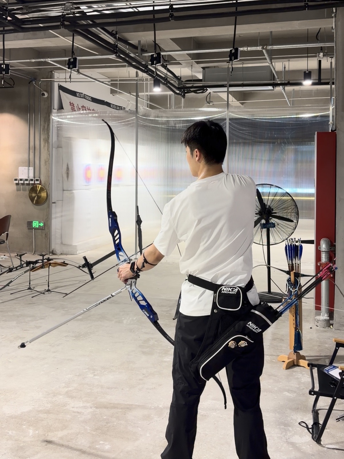 Zhuohan preparing a recurve bow at an indoor archery range