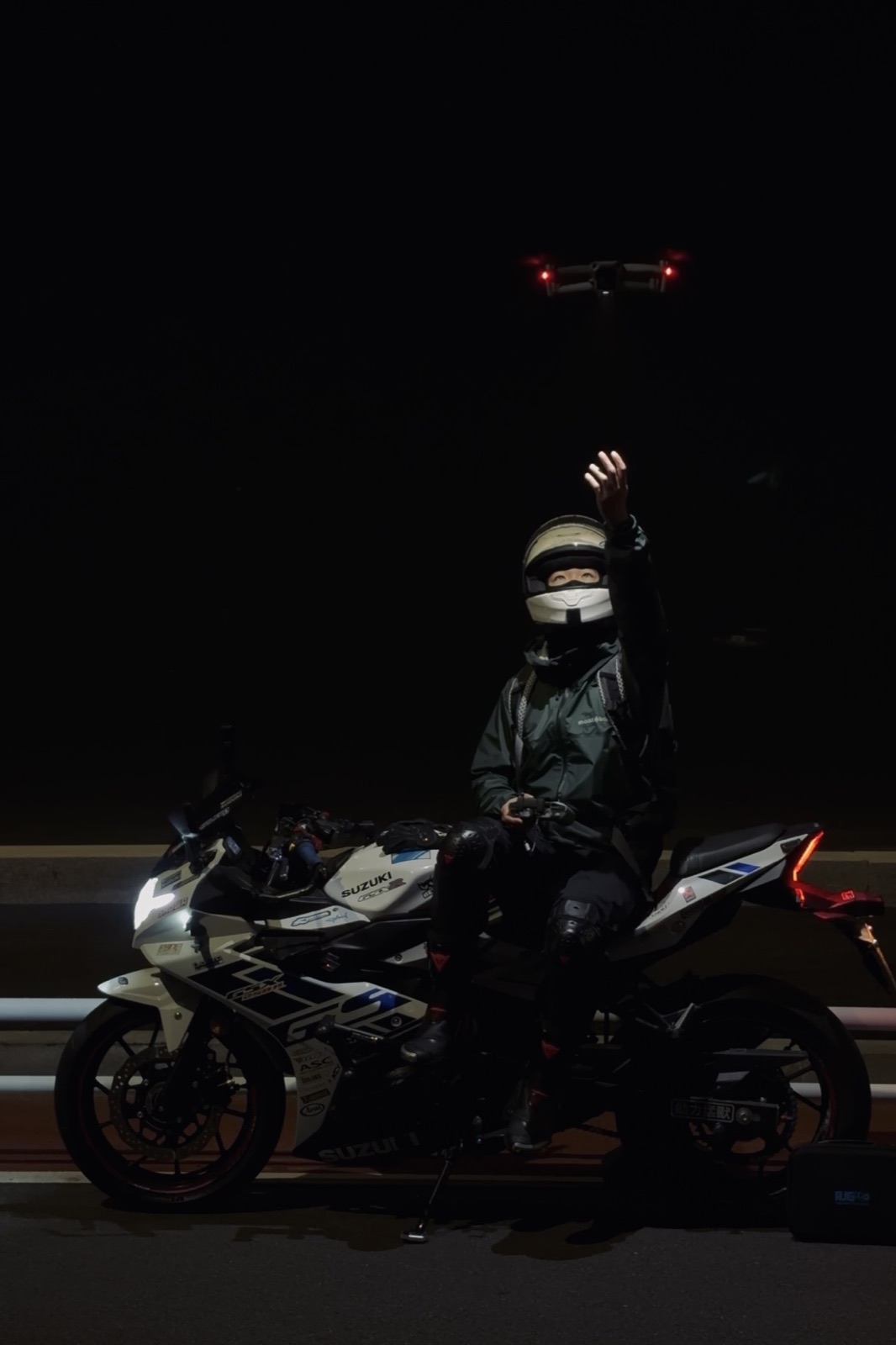 Zhuohan seated on a motorcycle beneath a hovering drone at night